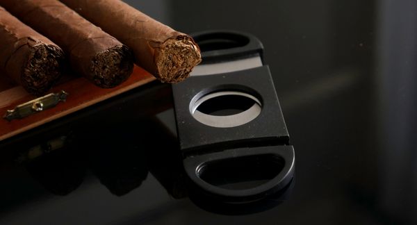 Three wedding cigars next to a cigar cutter accessory