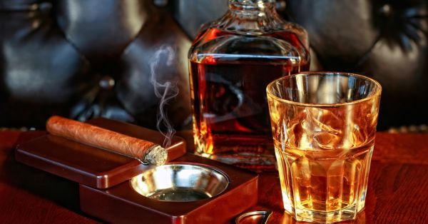 Cigar Burning in Ashtray on Table Next to Whiskey