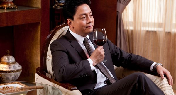 Man in suit drinking red wine with cigar burning in ash tray