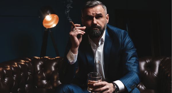 Man with Suit Smoking Cigar and Drinking Whiskey on Couch