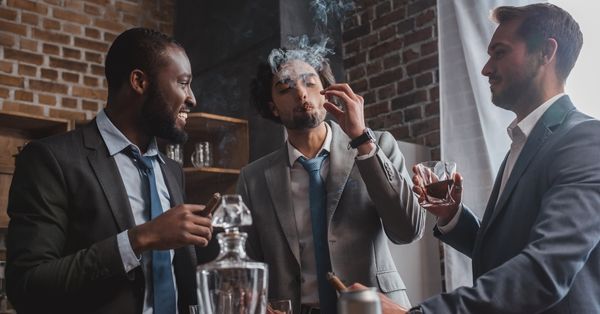 Three men in suits enjoying cigars and scotch while socializing